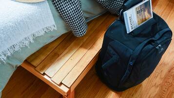 A bed with a white blanket and a black and white checkered blanket, a wooden nightstand, a black backpack, and a hat on the bed.