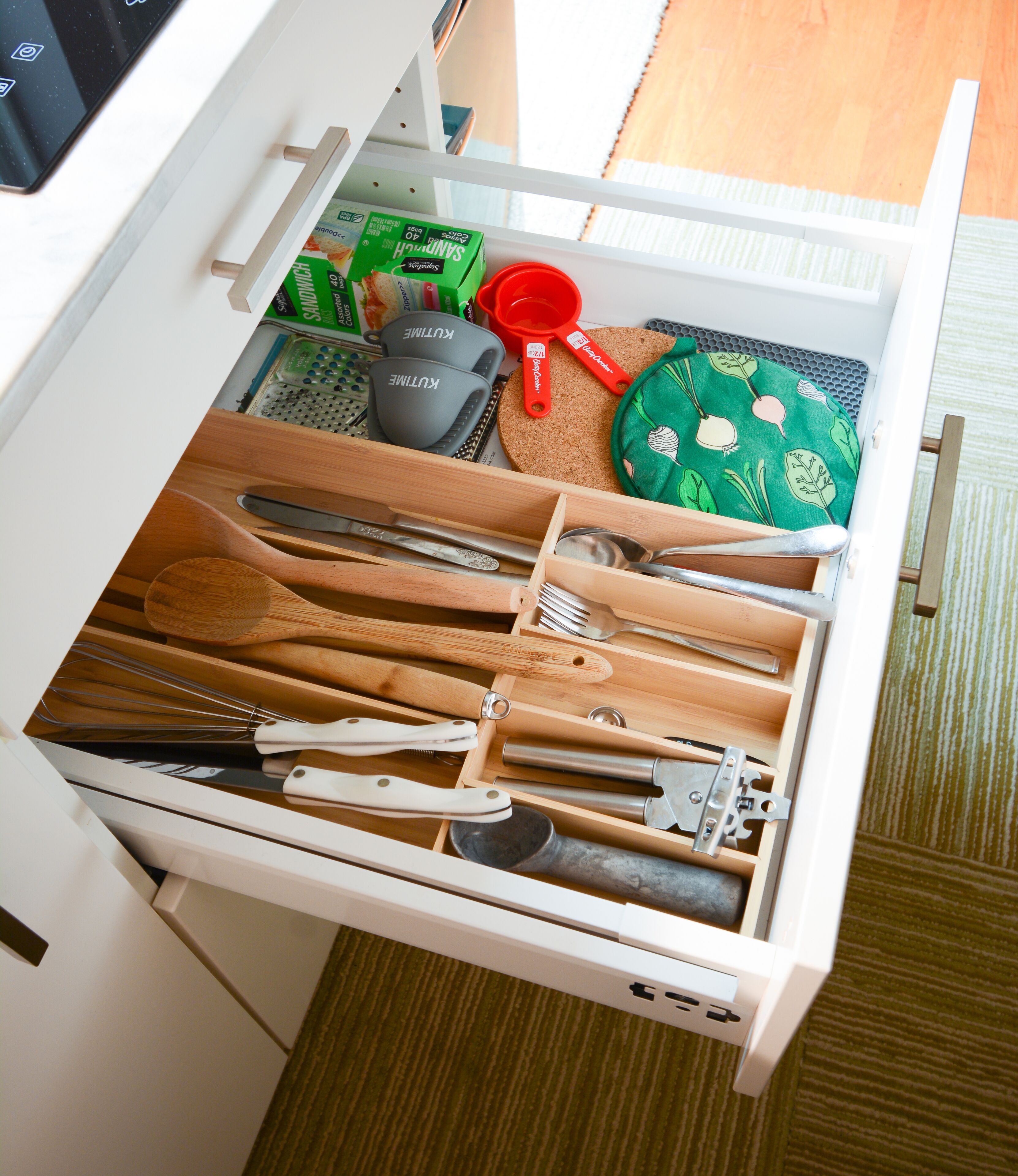 A kitchen drawer with utensils, a cutting board, and a green plate with a leaf pattern.