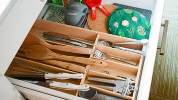 A kitchen drawer with utensils, a cutting board, and a green plate with a leaf pattern.