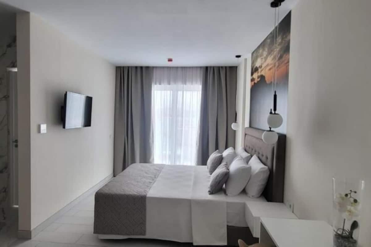 Een moderne hotelkamer met een marmeren wand, een bed met een grijze hoofdbord, een nachtkastje, een televisie en een raam met gordijnen.