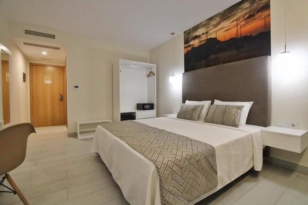 Een moderne hotelkamer met een groot bed, nachtkastje, kledingkast en een schilderij aan de muur.