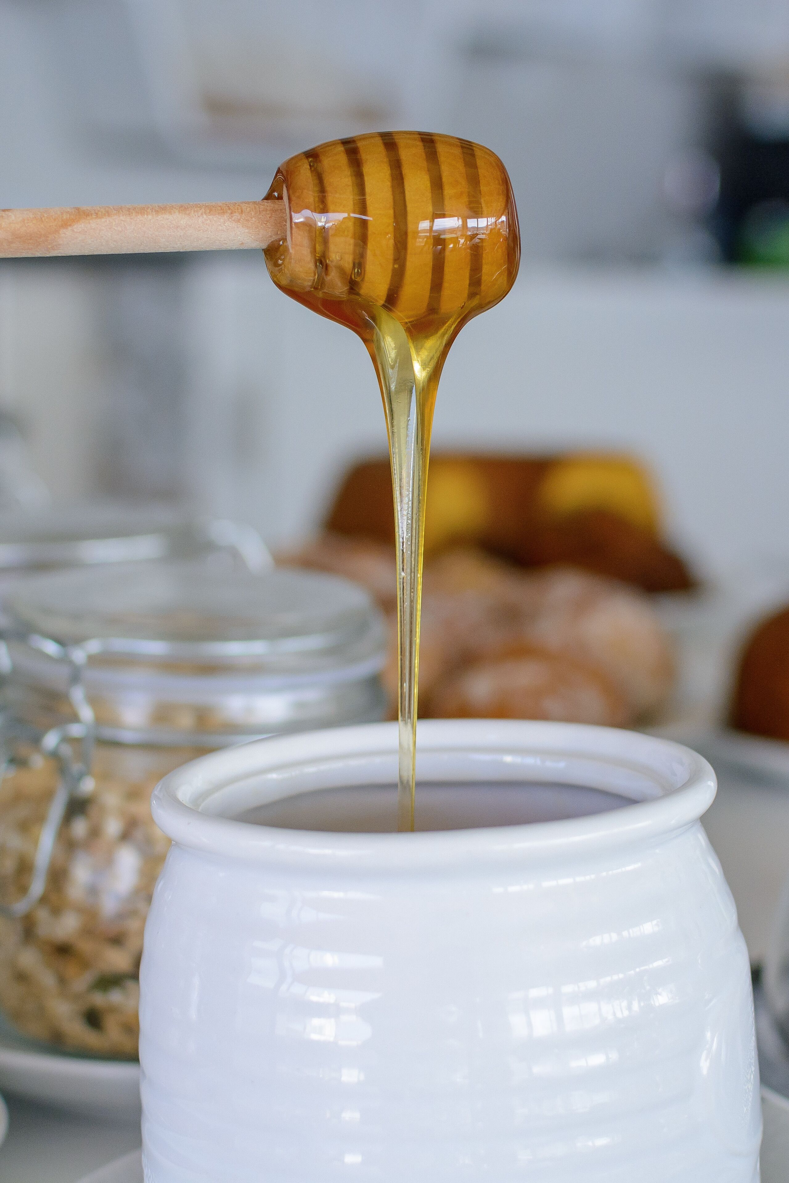 A honey dipper dripping honey into a white ceramic mug.