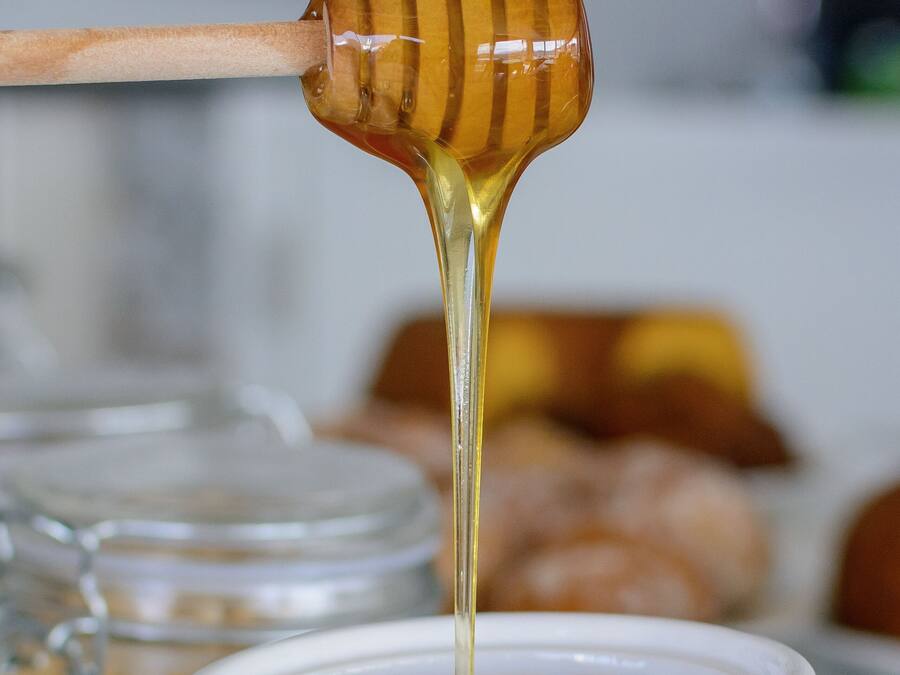 A honey dipper dripping honey into a white ceramic mug.