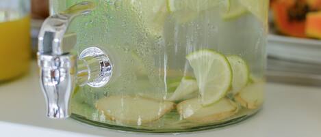 A glass pitcher with a tap, filled with a clear liquid and lime slices.