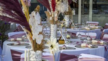 Une table dressée pour un événement formel, avec de la vaisselle blanche et dorée, des centres de table floraux et une structure en verre qui l’entoure.