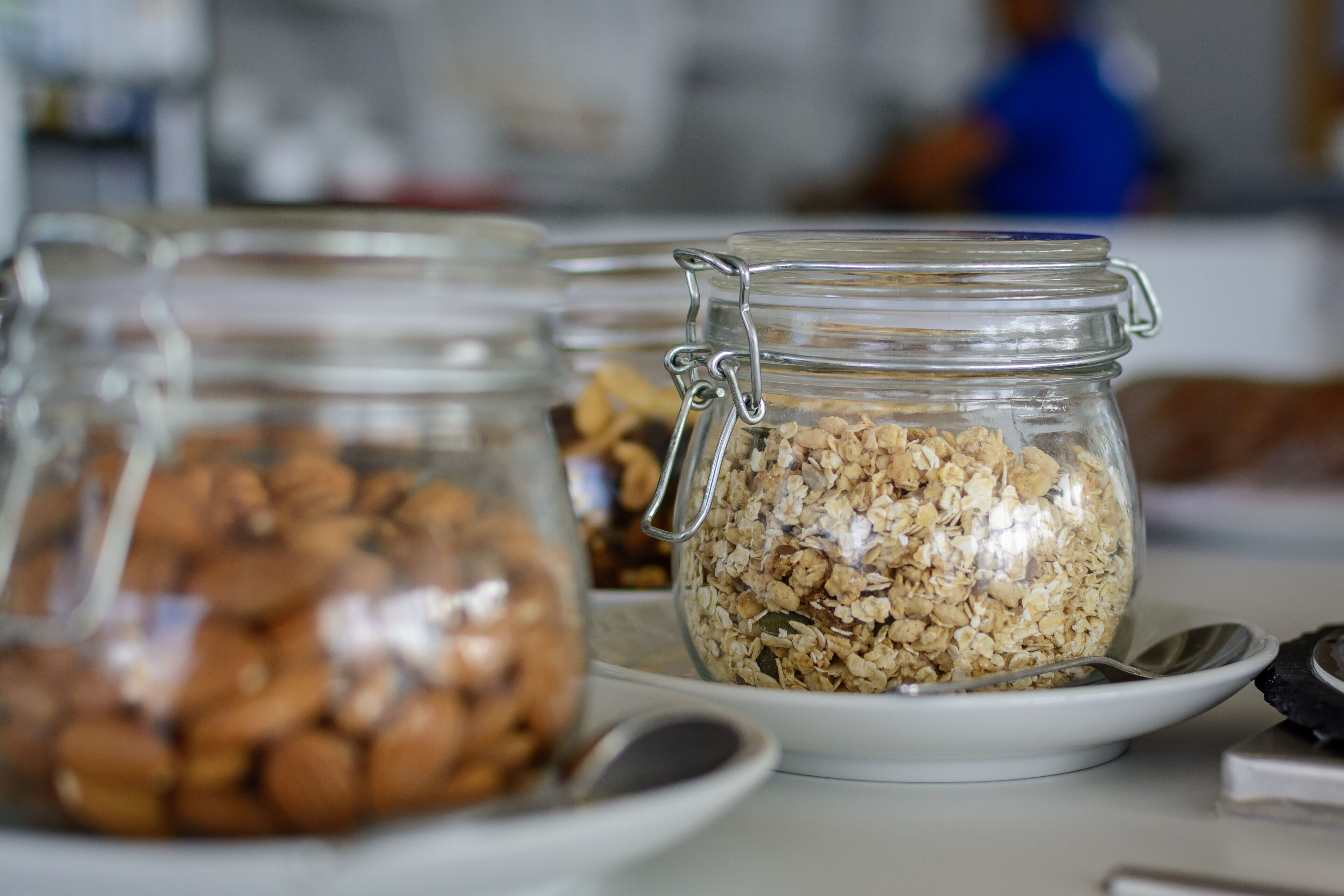 A breakfast buffet with various food items in glass jars, including granola and nuts, on white plates.