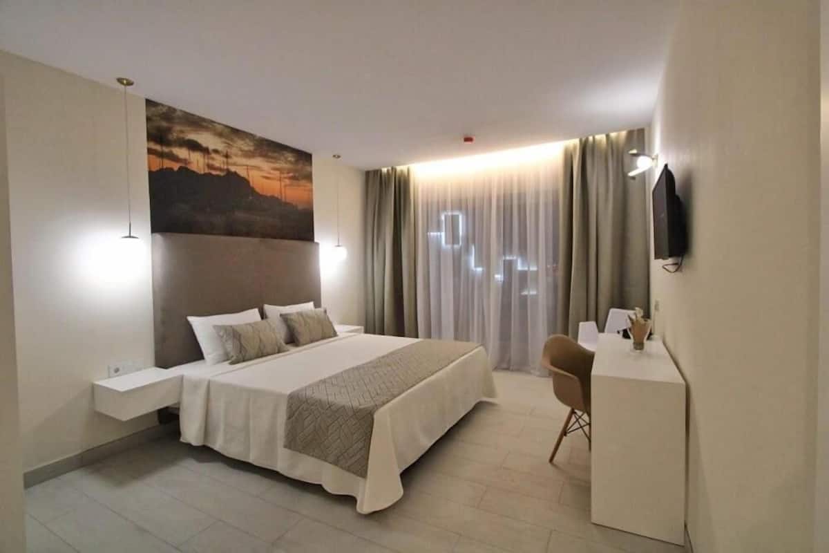 Een moderne hotelkamer met een groot bed, nachtkastjes, een bureau en een aan de muur bevestigde televisie.