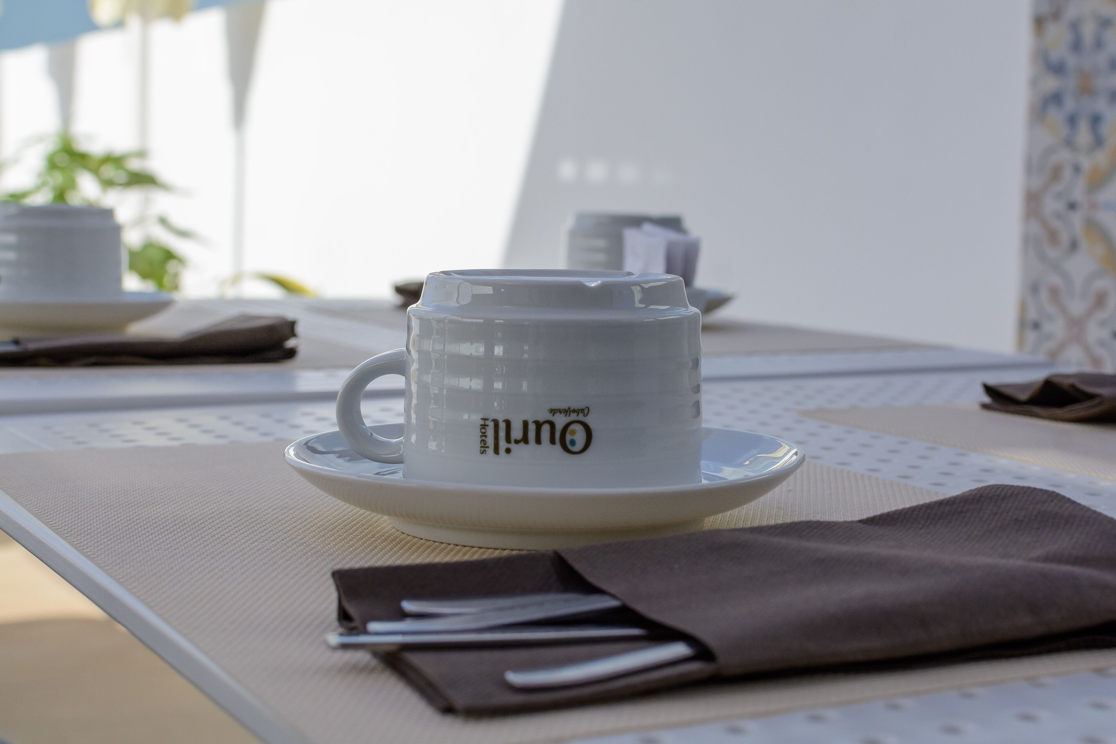 A white coffee cup with the word "hotel" on it, placed on a table with a napkin and a menu.