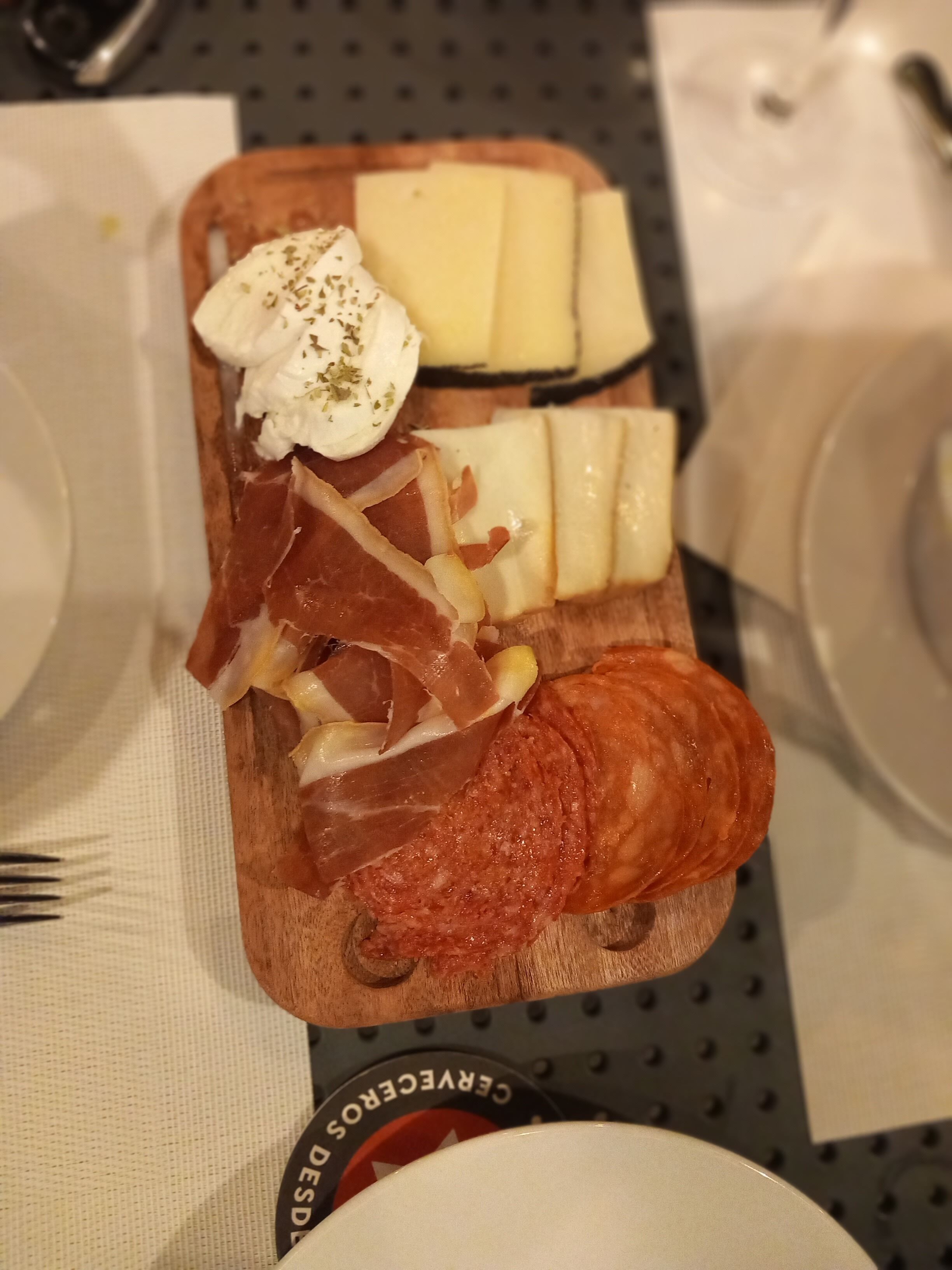 Una tabla de madera con varios quesos, embutidos y un pastel.