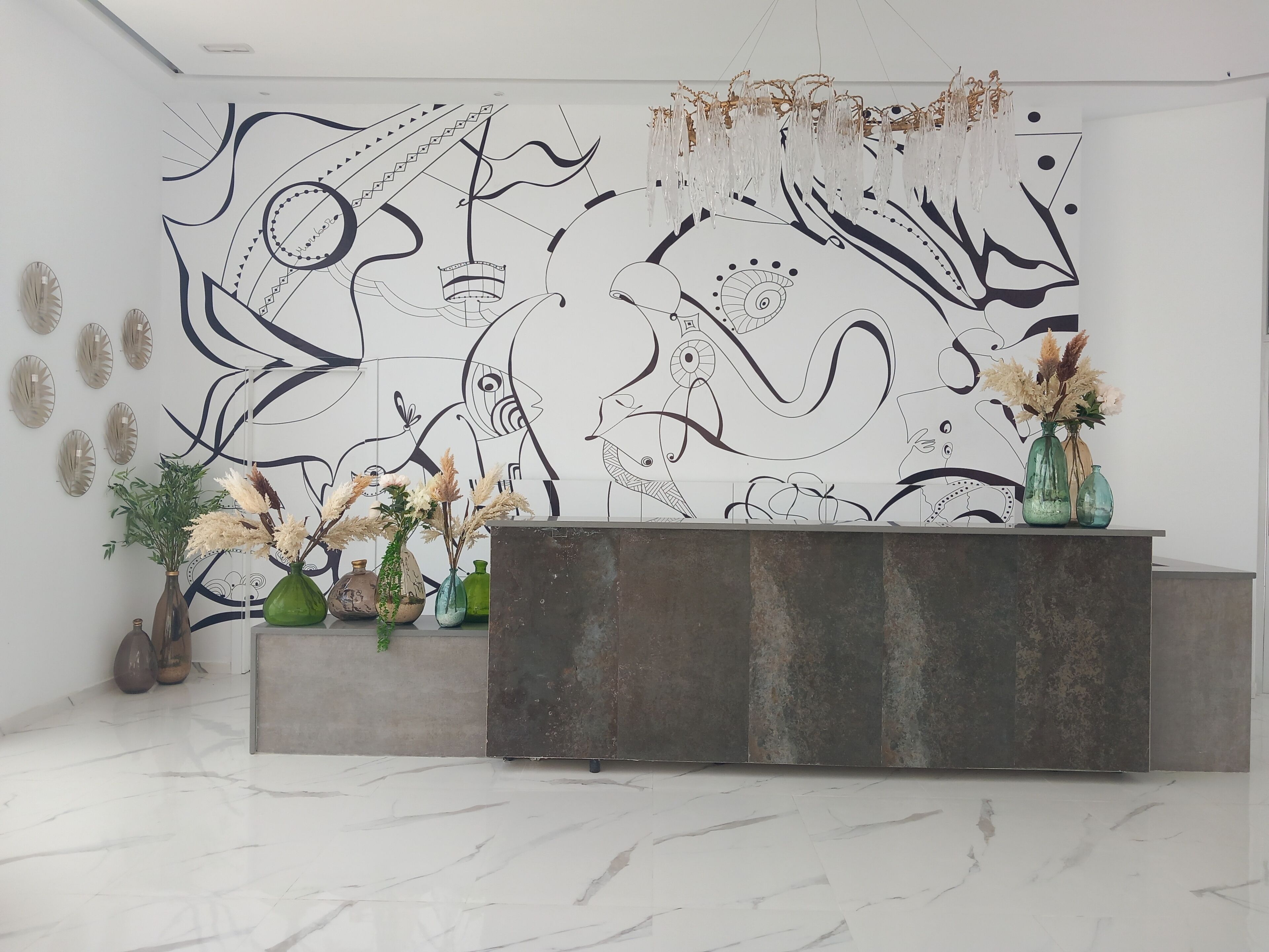 Uma área de recepção com design moderno, com piso de mármore, balcão de recepção e uma parede com arte abstrata.