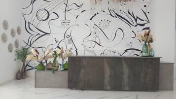 Uma área de recepção com design moderno, com piso de mármore, balcão de recepção e uma parede com arte abstrata.