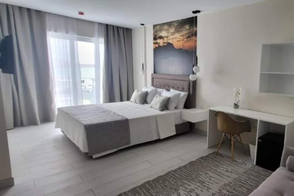 Een moderne hotelkamer met een groot bed, een bureau en uitzicht op zee.