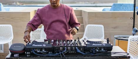 A DJ setup with Pioneer DJ equipment on an outdoor table, surrounded by white chairs, with a scenic view in the background.