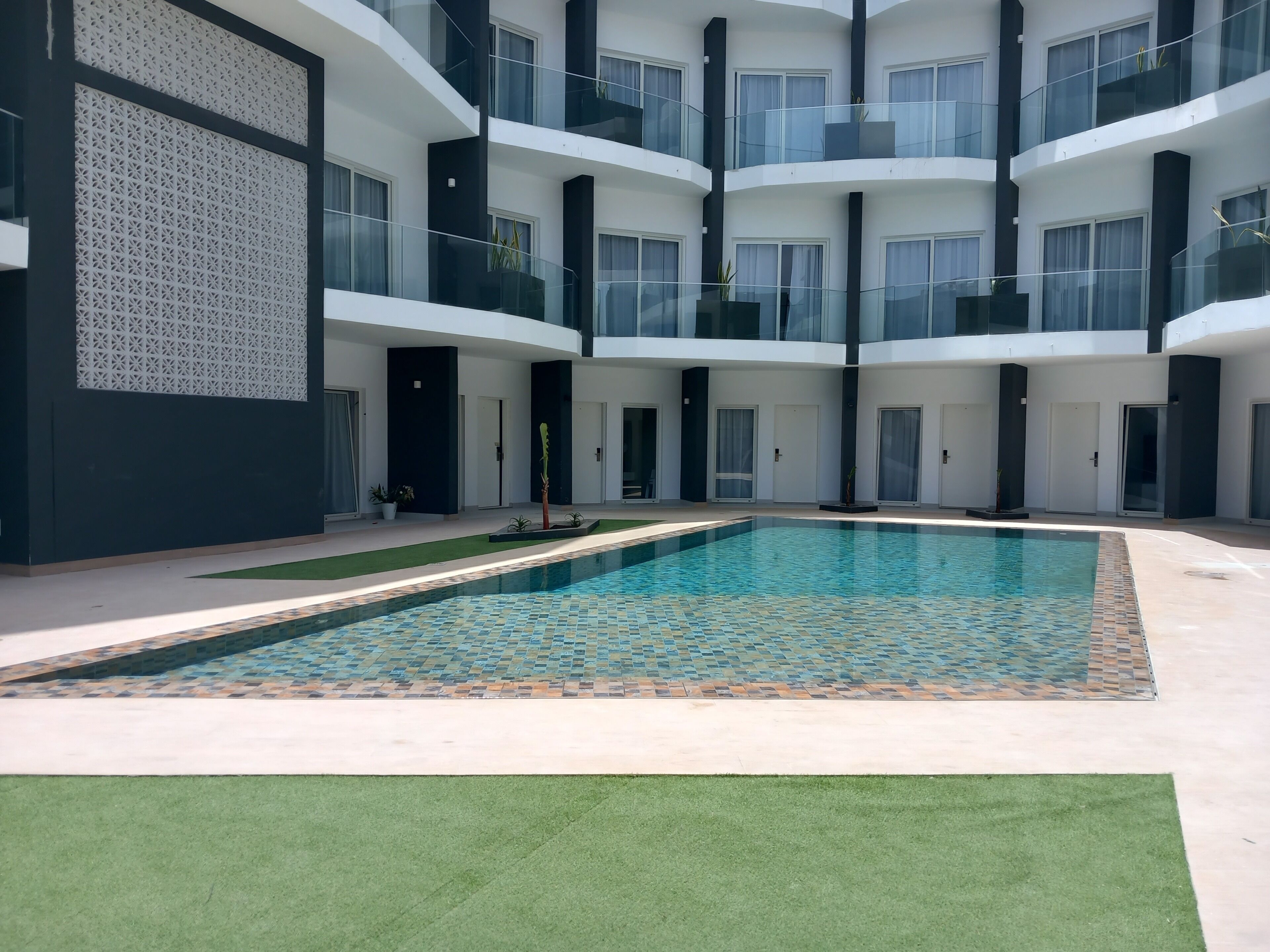En moderne bygning med flere etager, en central swimmingpool og altaner med gelændere af glas.
