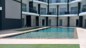 A modern multi-story building with a central swimming pool, surrounded by balconies with glass railings.