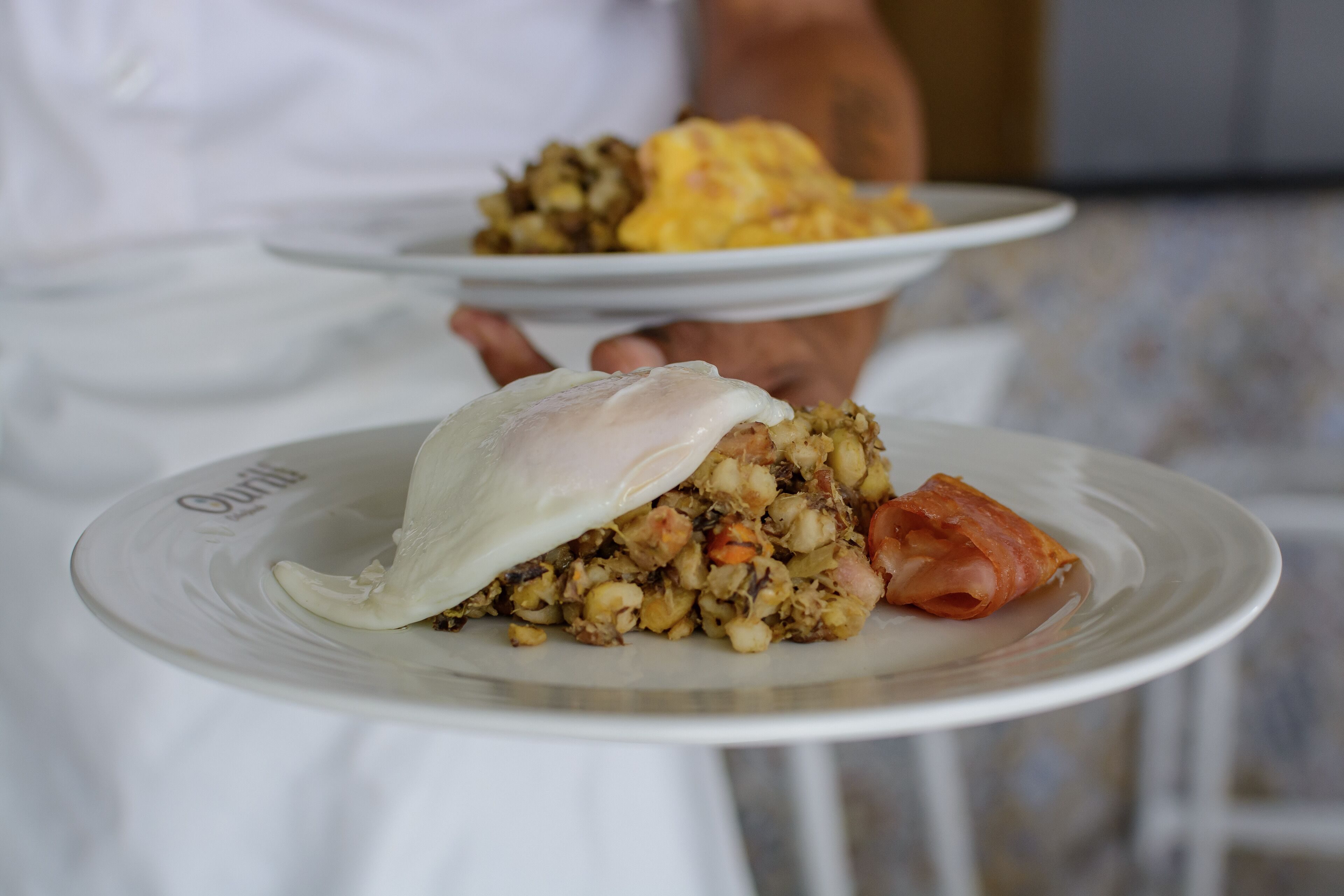 A person holding a plate with a dish that includes a poached egg and a mix of vegetables and meat.