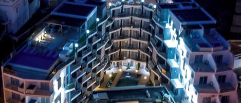 A multi-story hotel with a central courtyard, balconies, and a parking area.