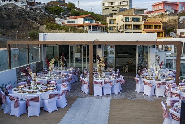 Un área de comedor al aire libre con mesas y sillas redondas, preparada para un evento formal.