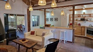 A cozy living room with a sofa, a coffee table, and hanging lights. There is a kitchen area with a refrigerator, stove, and bar stools. - Casa Tarif - Bolonia Beach Campus, your beach house in Bolonia - Tarifa (Tarifa)