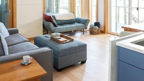 Una sala de estar moderna con techo de madera, ventanas amplias y un sofá gris.