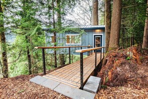 A wooden deck leading to a cabin in a forested area. - Bellingham Treehouse w/ Waterfall, View, & Hot Tub (Bellingham)