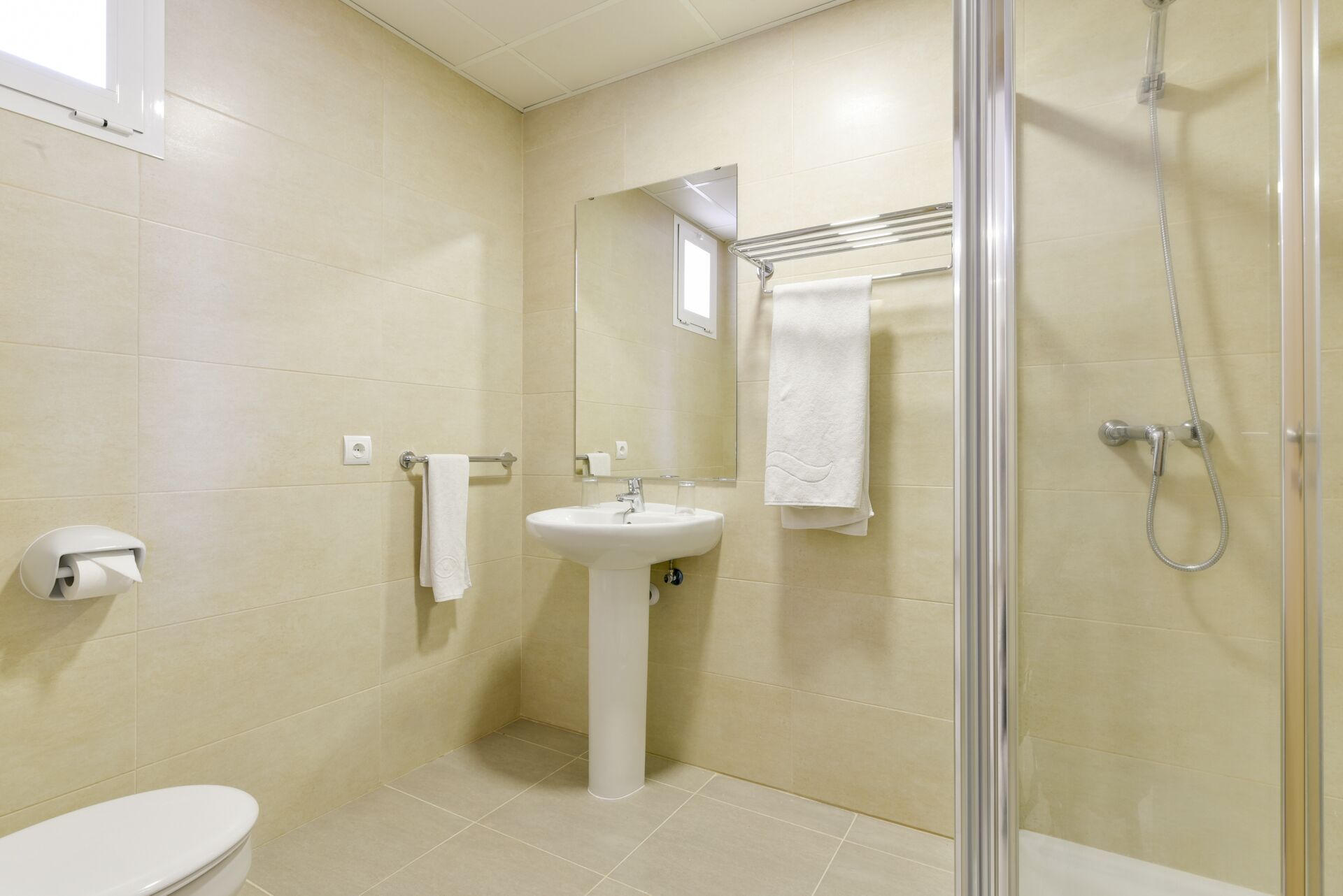 Un baño con inodoro, lavamanos, espejo, toallero y ducha.
