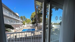Blick auf einen Swimmingpool von einem Balkon mit Metallgeländer, umgeben von Gebäuden und Bäumen.