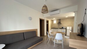 Ein modernes Wohnzimmer mit einer Couch, einem Esstisch, Stühlen, einem Fernseher und einer Küchenzeile mit Geräten.