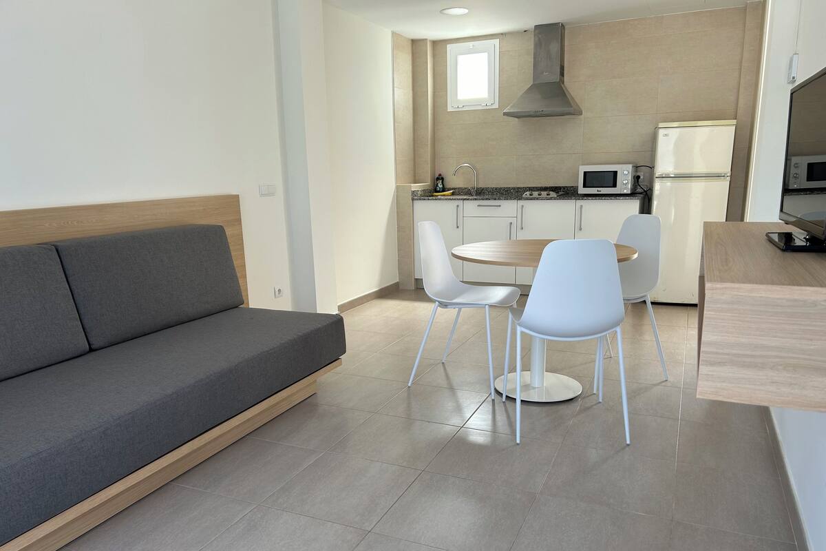 Una cocina moderna con comedor, que incluye un sofá gris, sillas blancas y una mesa de madera.