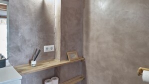 A bathroom with a wooden ceiling, a hanging lantern, a trash bin, and a shelf with toilet paper and a small container. - Bungalow - Bolonia Beach Campus Bolonia, your beach house (Tarifa)
