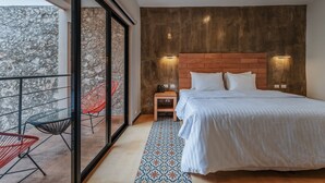A bedroom with a large bed, a wooden headboard, two bedside tables with lamps, a patterned rug, and a balcony with chairs. - Hotel Casa 57 (Mérida)