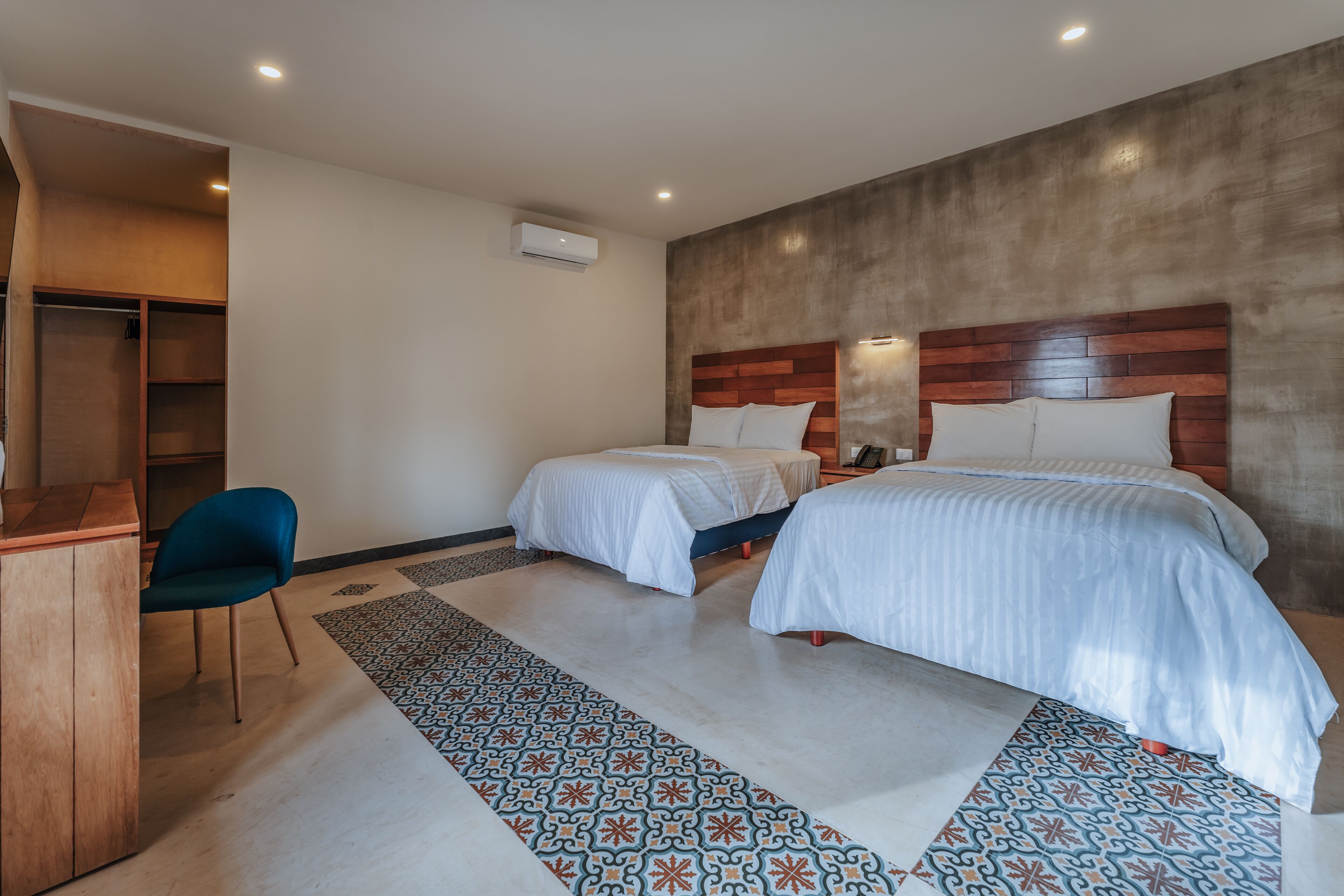 A hotel room with two beds, a desk, a chair, and a patterned rug.