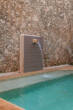 A pool with a stone wall and a tiled wall with a water feature.