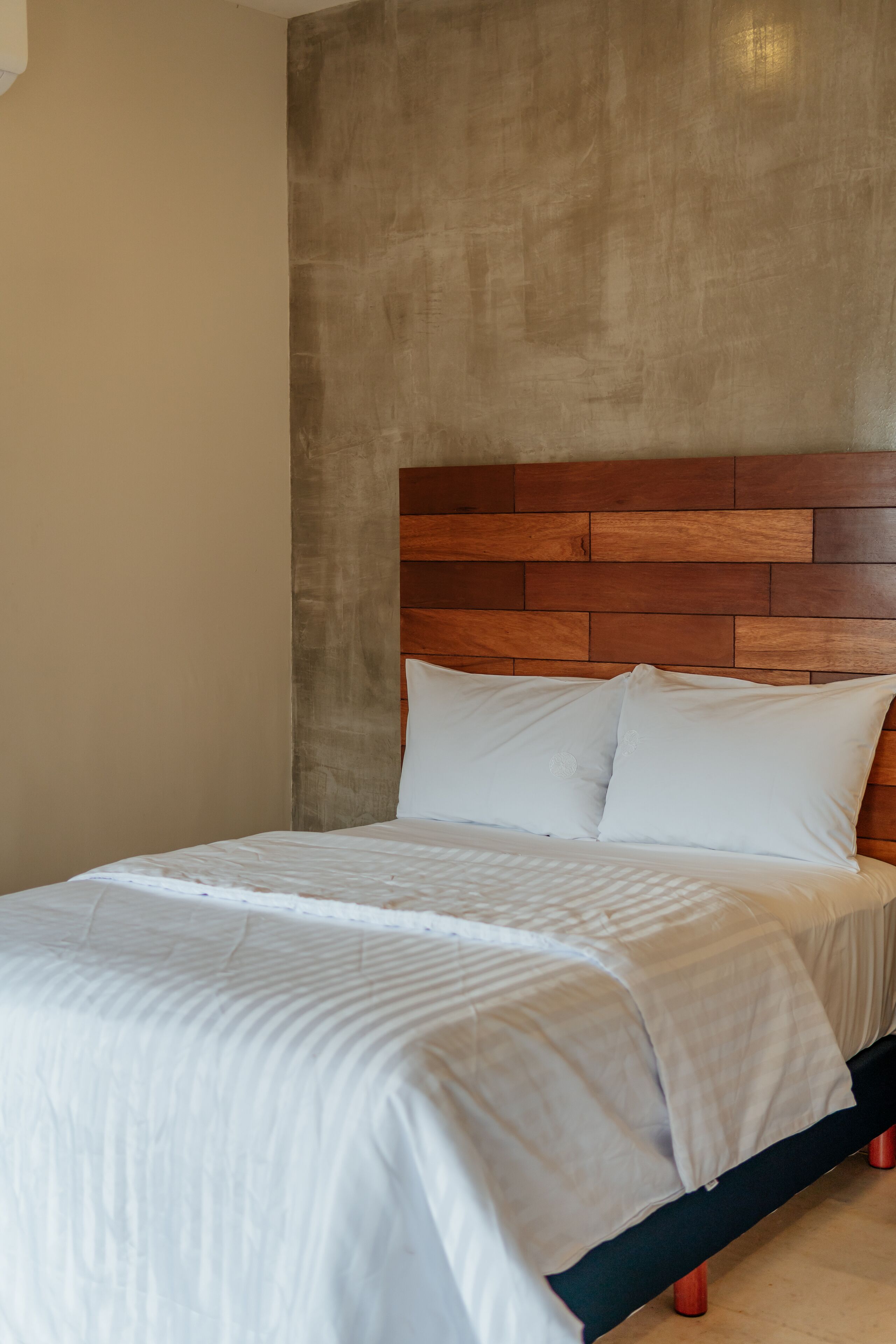 Una cama con cabecera de madera, ropa de cama blanca y piecera oscura.