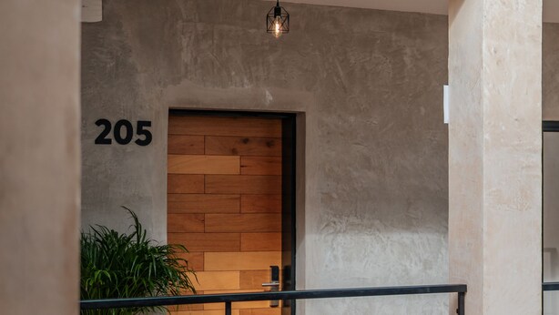 A modern apartment with a wooden door, a balcony with a railing, and a potted plant. - Hotel Casa 57 (Mérida)