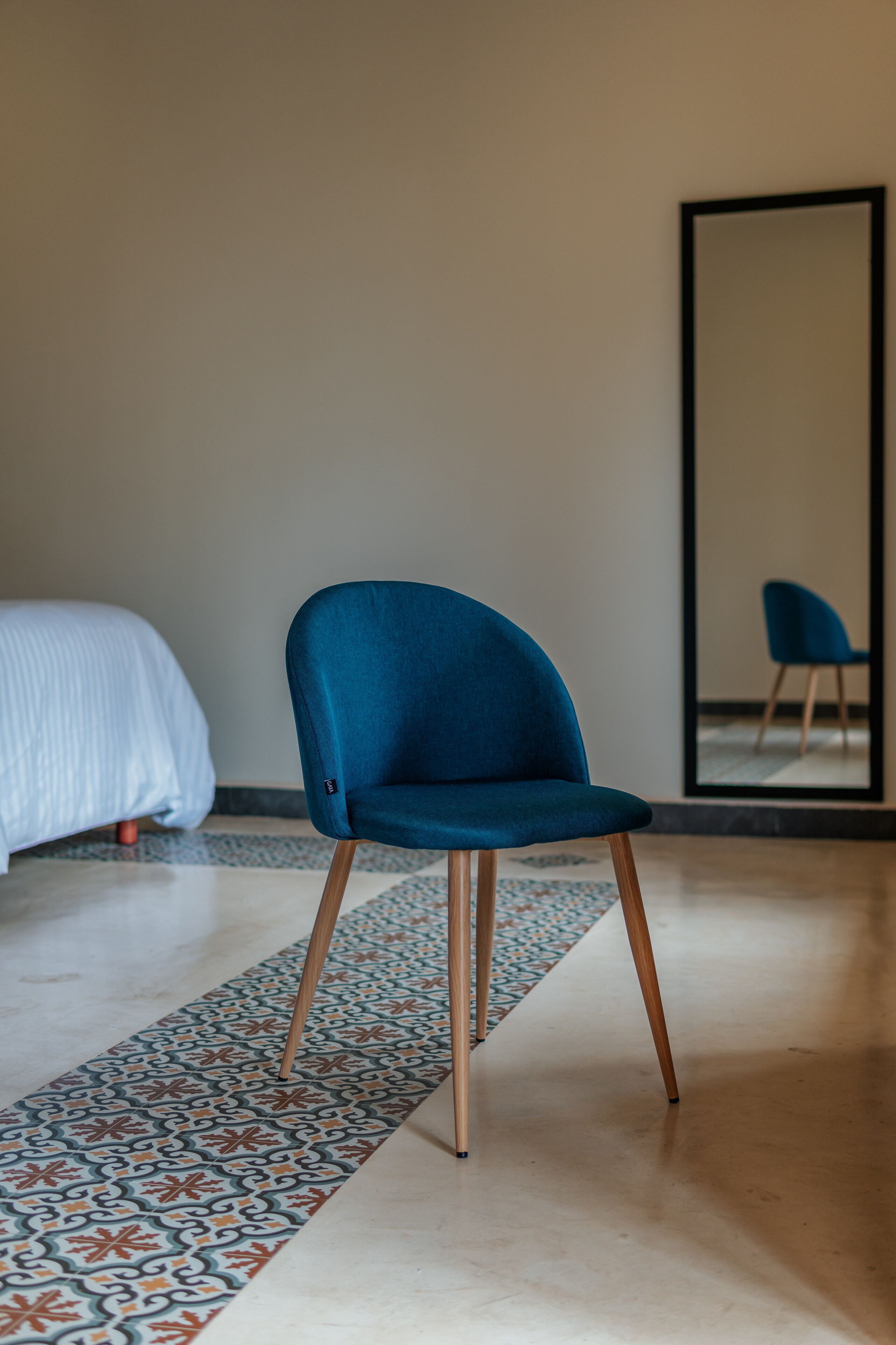 A modern room with a blue chair, a bed with white bedding, and a patterned rug.