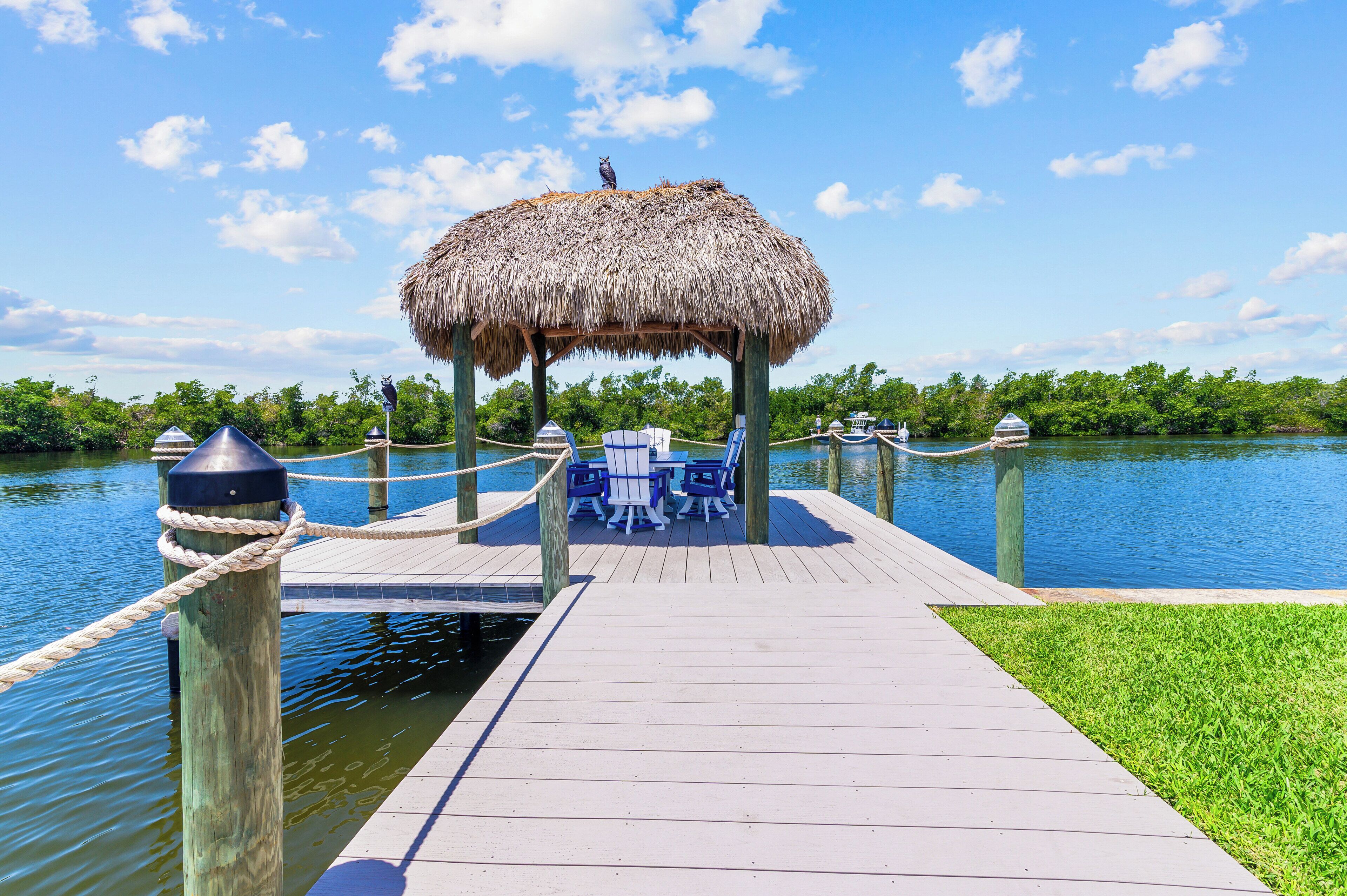 A wooden dock with a thatched-roof structure, a table with chairs, and a rope barrier.