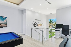 Een moderne hotelkamer met een pooltafel, een bureau met een computer en inspirerende muurkunst.