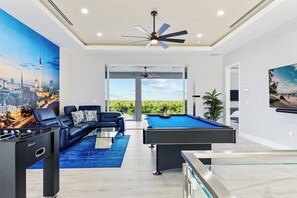 Een moderne woonkamer met een pooltafel, een zithoek en een muurschildering van een stadsgezicht.