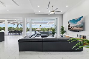 Een moderne woonkamer met een grote hoekbank, een plafondventilator en uitzicht op een zwembad en terras.