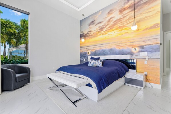 Un dormitorio moderno con una cama grande, vistas al exterior a través de una ventana y un mural del atardecer en la pared.