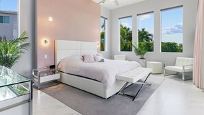Ein modernes Schlafzimmer mit einem großen Bett, einem Deckenventilator und Blick auf Grünflächen.