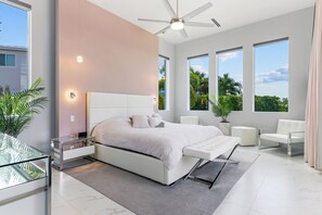 Een moderne slaapkamer met een groot bed, een plafondventilator en uitzicht op groen.