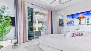 Een moderne slaapkamer met een groot bed, een glazen schuifdeur naar een balkon en uitzicht op de stad.