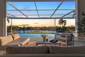 A modern outdoor seating area with a pool, overlooking a body of water and a sunset view.