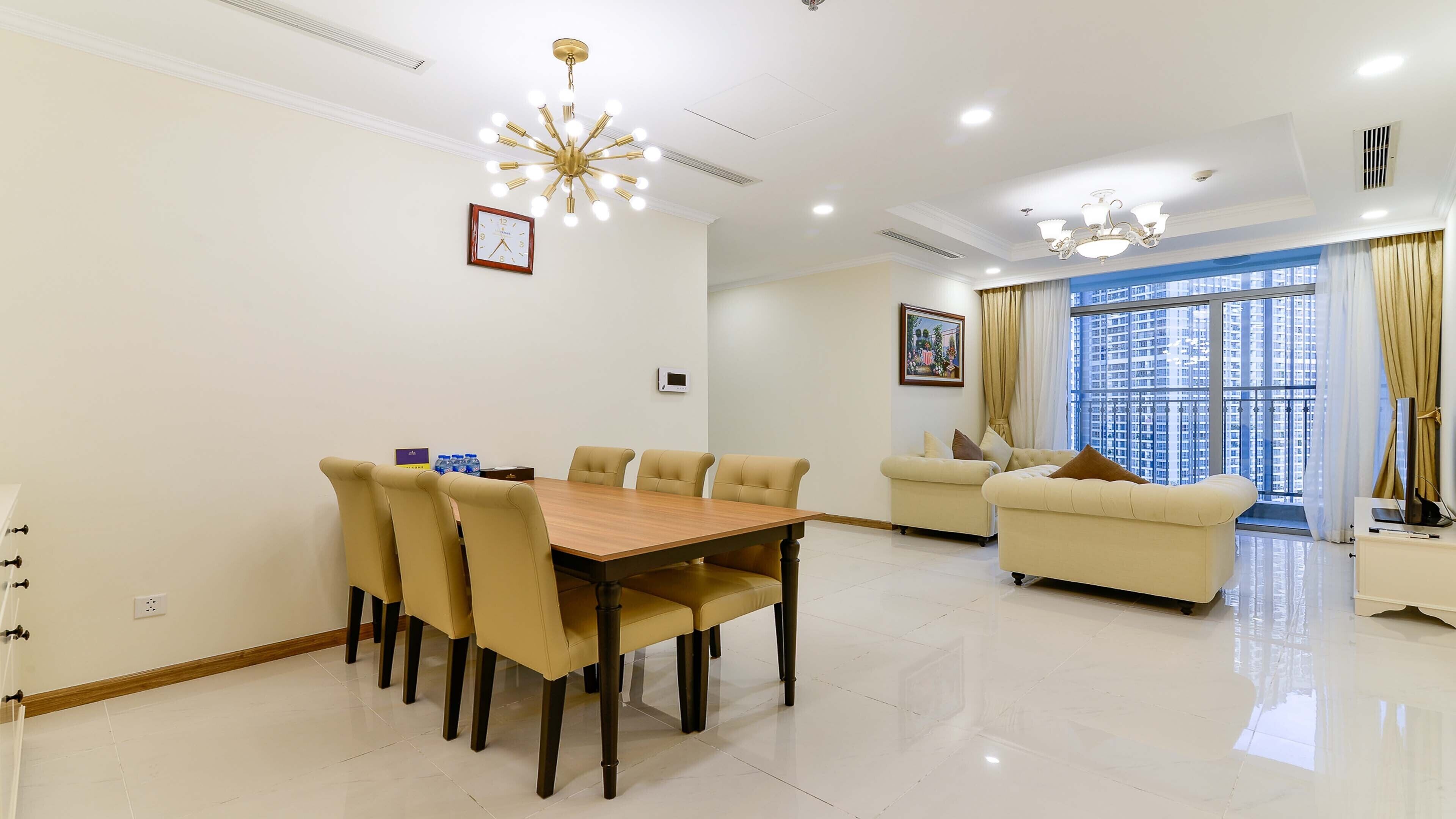 A modern living room with a dining area, featuring a wooden dining table, beige sofas, and a large window with a city view.