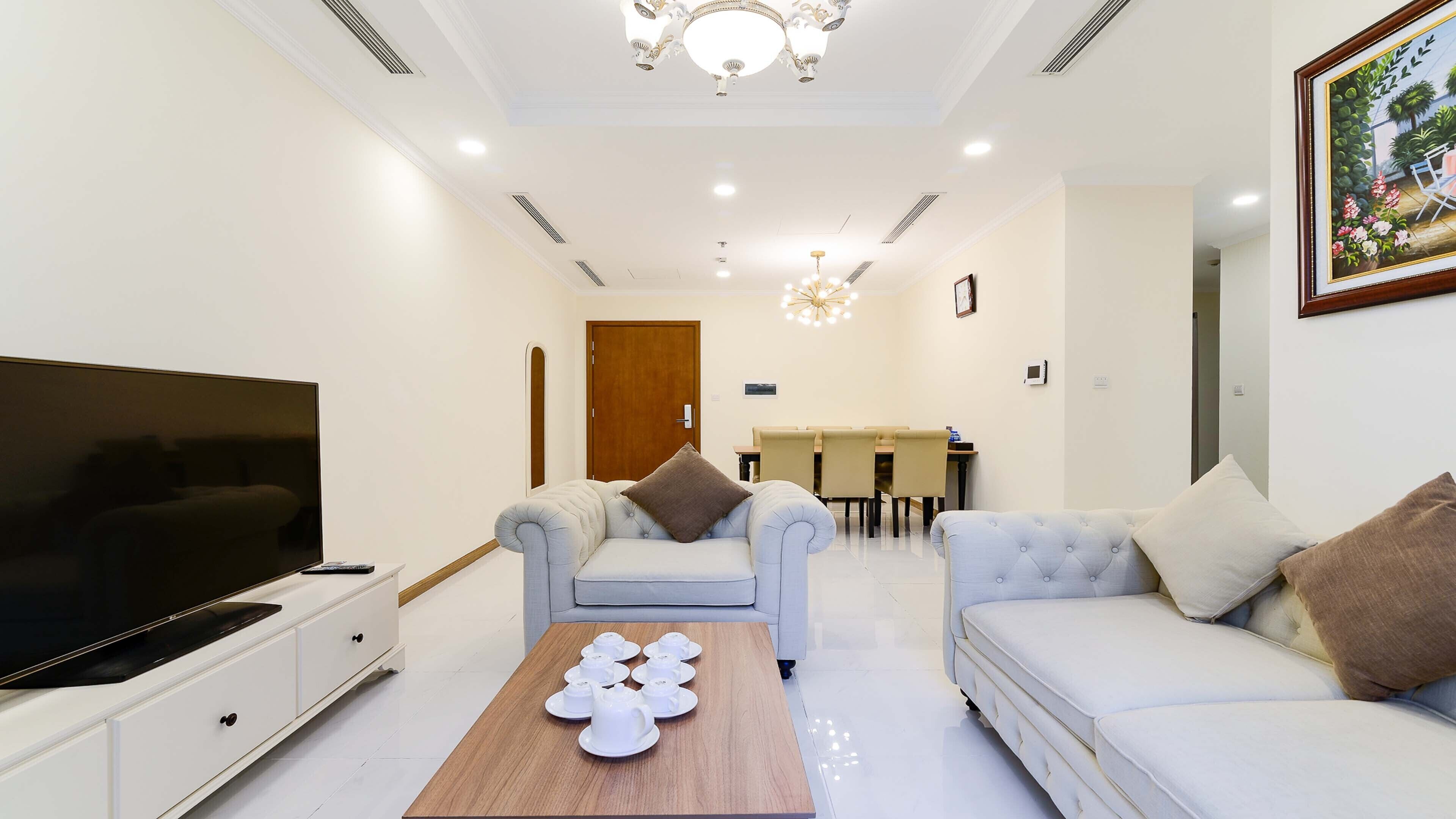 A modern living room with a flat-screen TV, two sofas, a coffee table, and a dining area with a table and chairs.