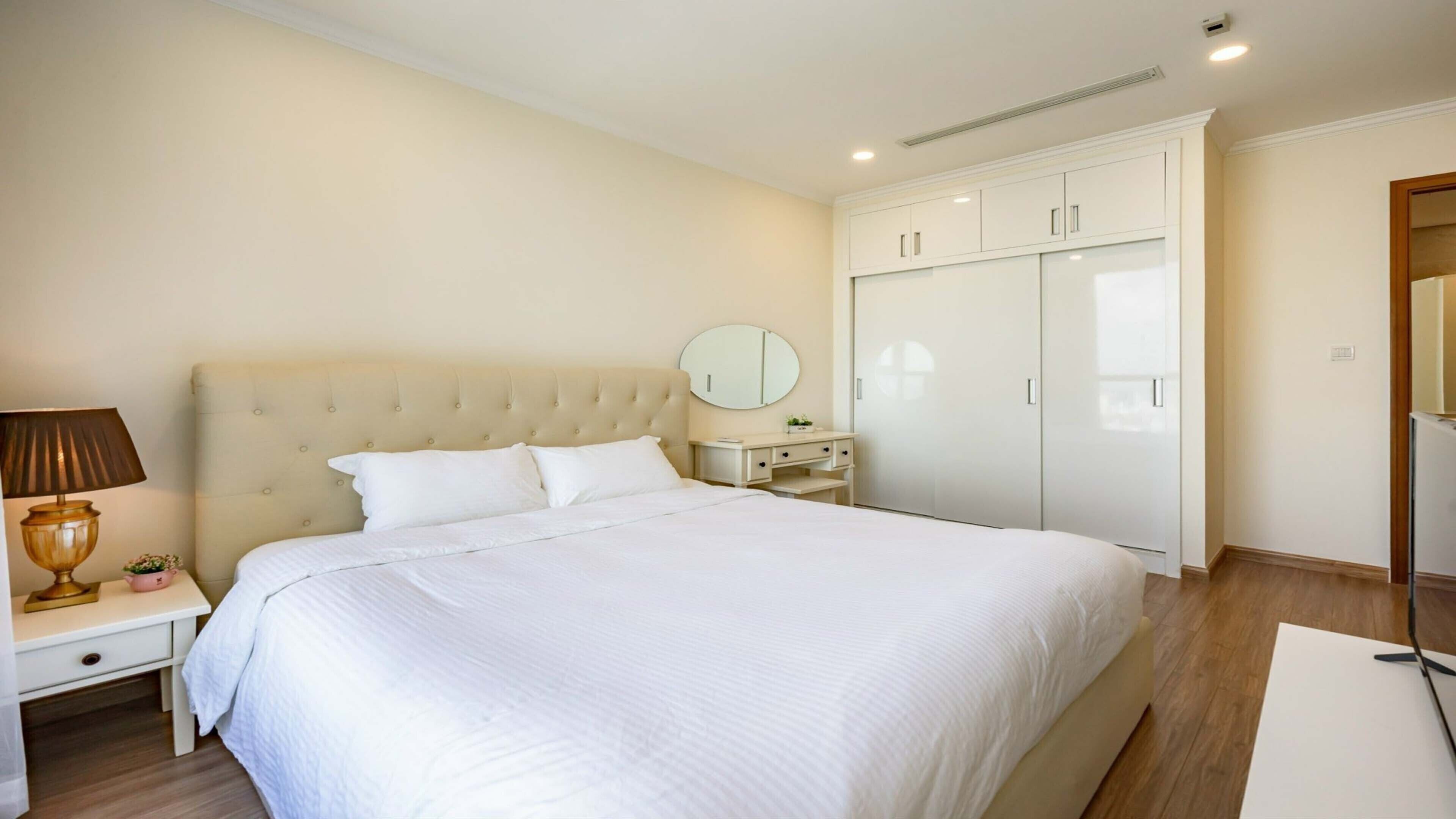 A bedroom with a large bed, a bedside table with a lamp, a dresser, and a wardrobe.