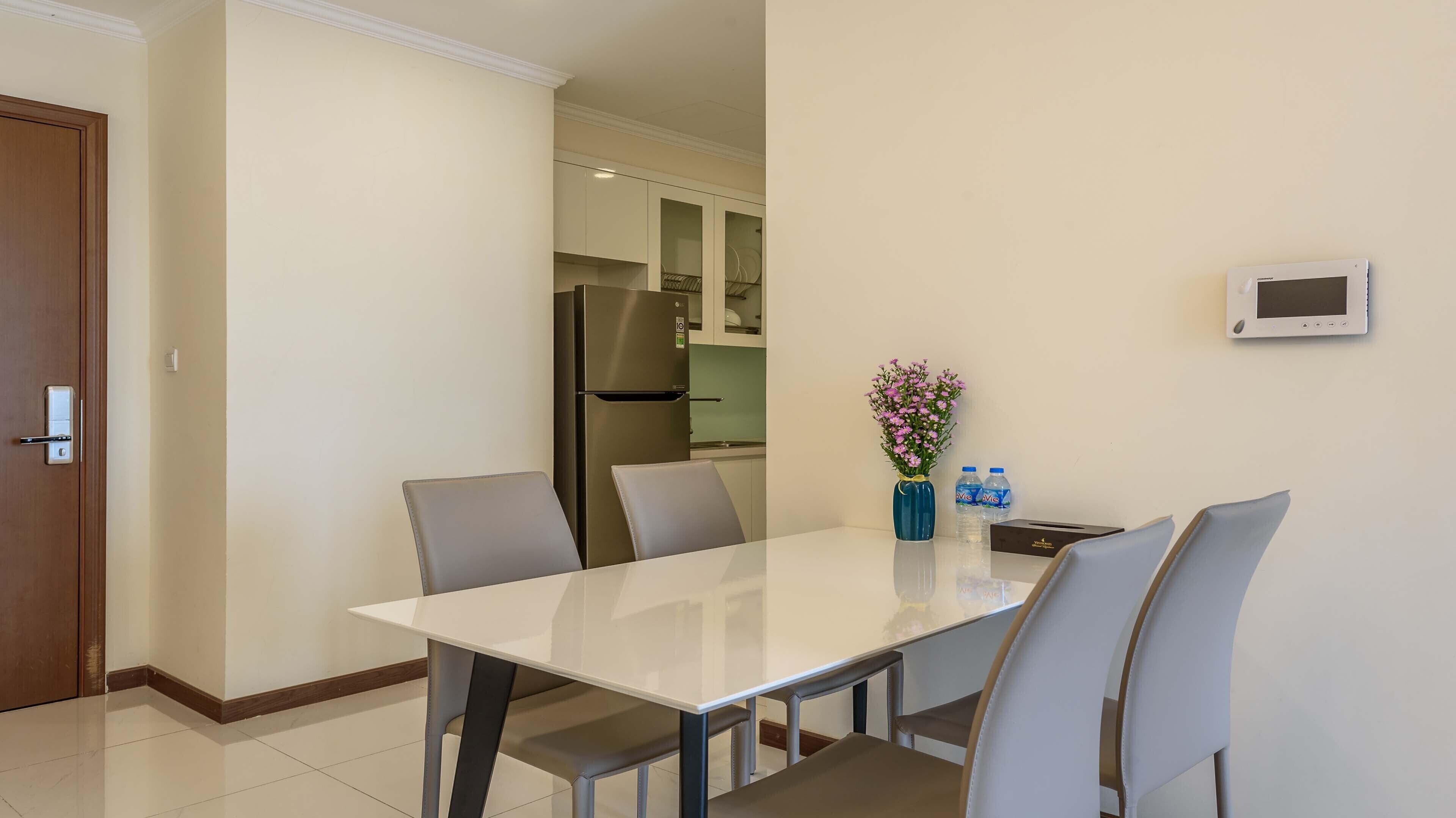 A dining area with a white table, four chairs, a vase with flowers, and a water dispenser.