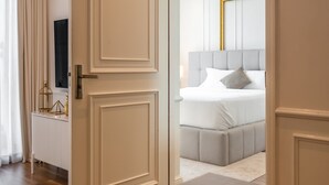 Ein Hotelzimmer mit Holzboden, einer weißen Tür, einem Bett mit grauem Kopfteil und einer großen Uhr an der Wand.